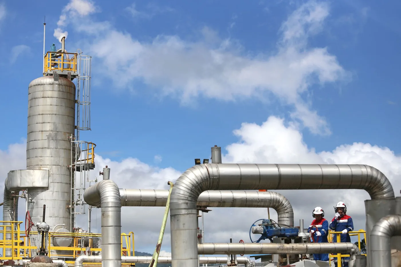 Two operators in safety gear working at a valve station on a gas processing plant